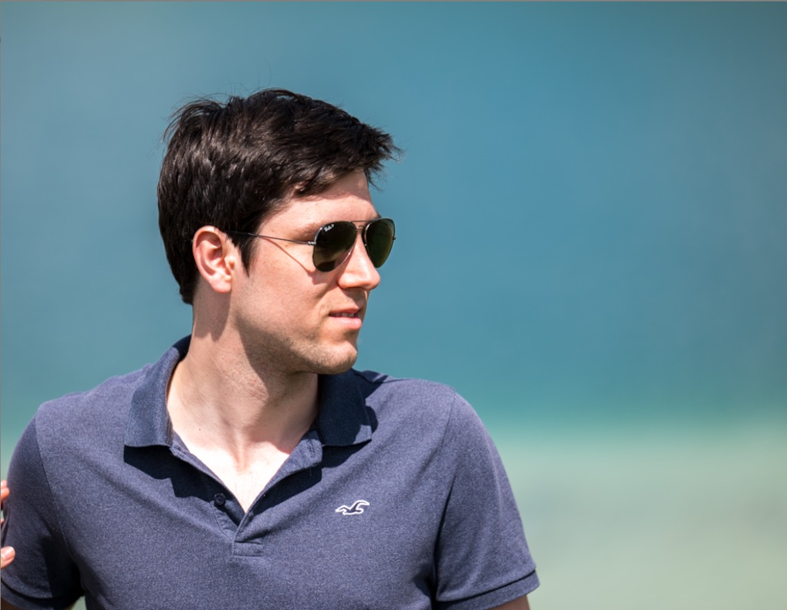 Stephen sitting beside a bright blue mountain lake